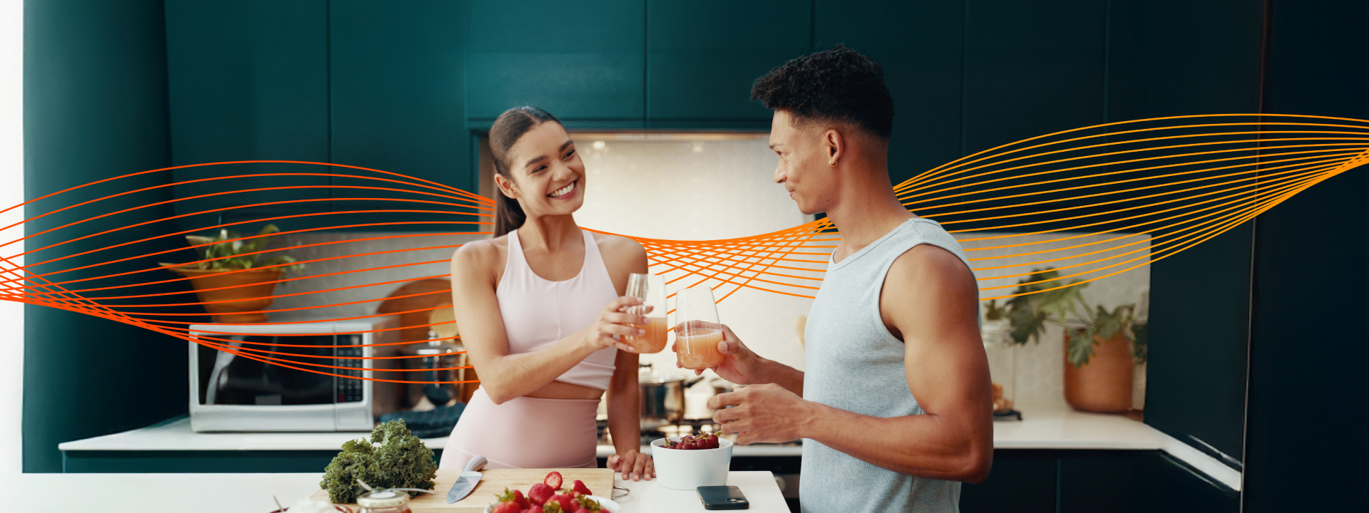 Casal saudável brindando com bebida clara na cozinha de casa, com frutas na bancada, representando hábitos equilibrados e nutrição.