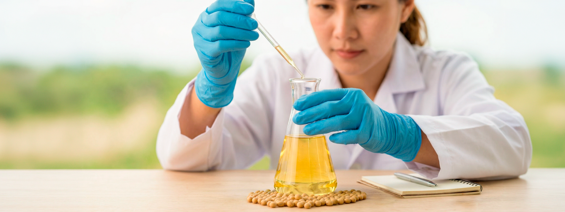 Cientista em laboratório manipulando óleo vegetal em frasco com pipeta, com grãos de soja ao redor — conceito de pesquisa, inovação e análise de matérias-primas naturais.